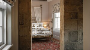 A bedroom with a metal bed frame, a patterned carpet, and a stone wall. - King William Pub with Rooms (Bath)