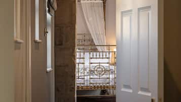 A narrow hallway leading to a room with a bed, a white door, and a stone wall.