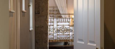 A narrow hallway leading to a room with a bed, a white door, and a stone wall.