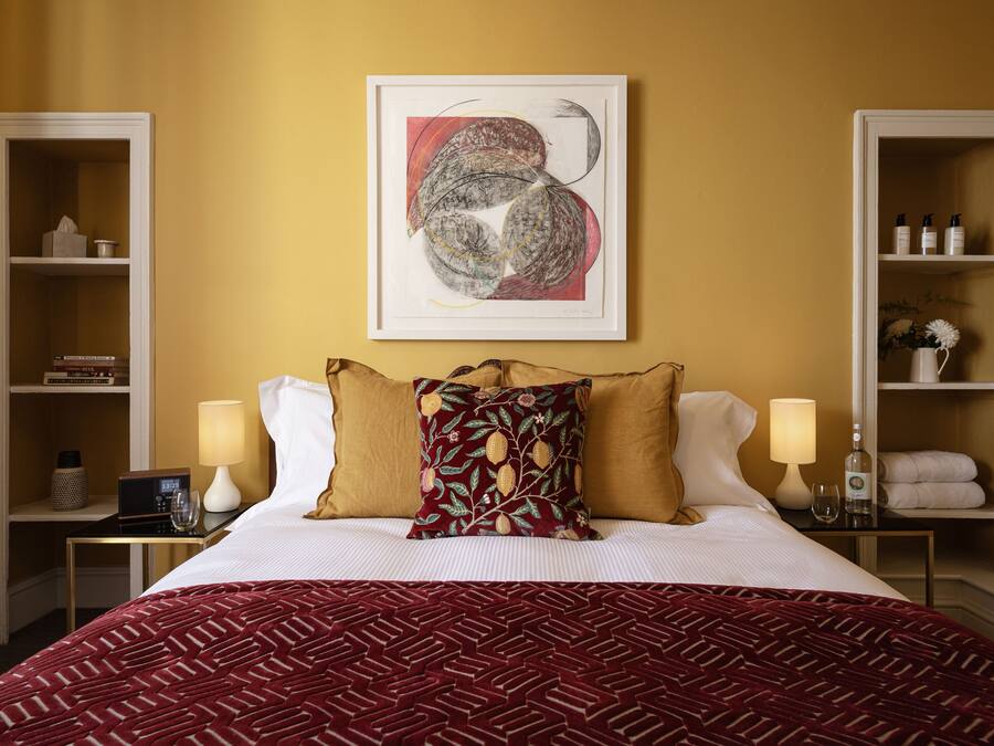 Habitación de hotel con una cama grande, dos mesitas de noche, un cuadro abstracto enmarcado y un armario con estantes.