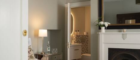 A hotel room with a bed, bedside table, lamp, and a fireplace.