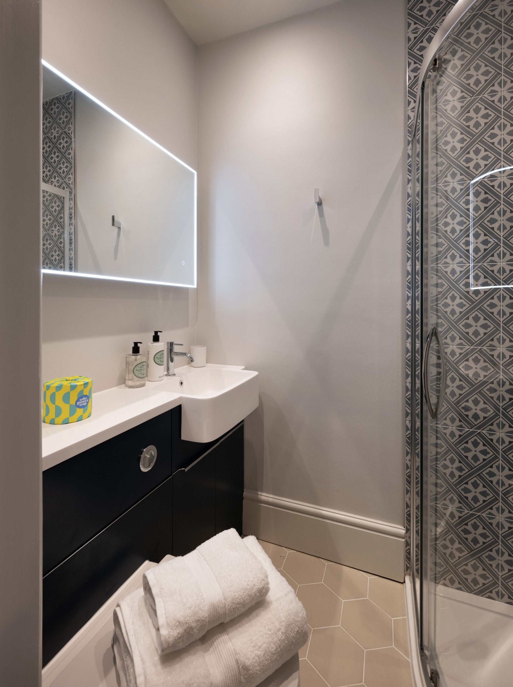 A modern bathroom with a white sink, black cabinet, and a glass shower enclosure.