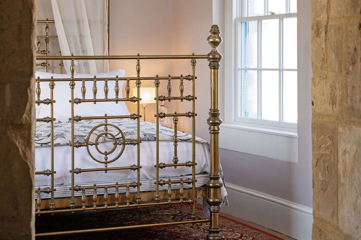 A room with a bed, a window with floral curtains, and a patterned carpet.
