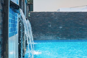 Una piscina con agua cristalina, un muro de azulejos y una estructura de piedra al fondo.