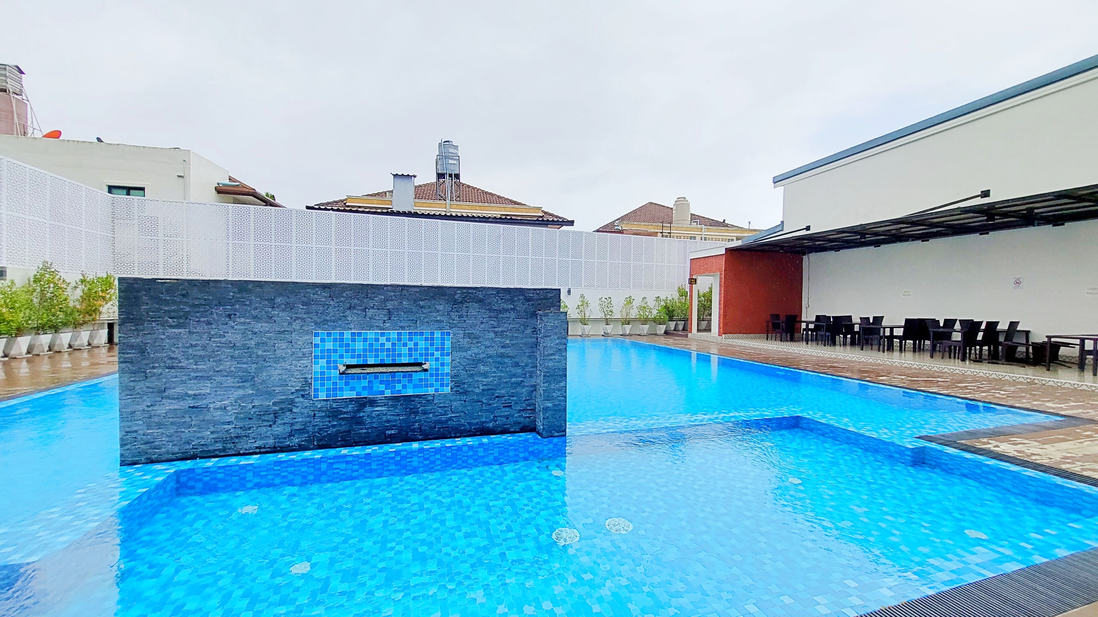 Una piscina con borde de azulejos, un muro de piedra con sección de azulejos azules y mobiliario exterior.