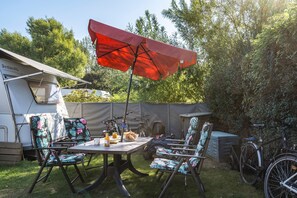Um local de camping com mesa, cadeiras, um guarda-sol vermelho e bicicletas.