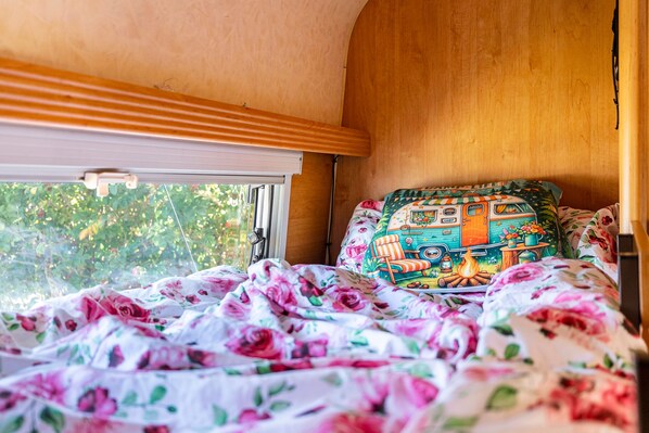 A bed with floral bedding, a colorful pillow, and a window with a view of greenery.