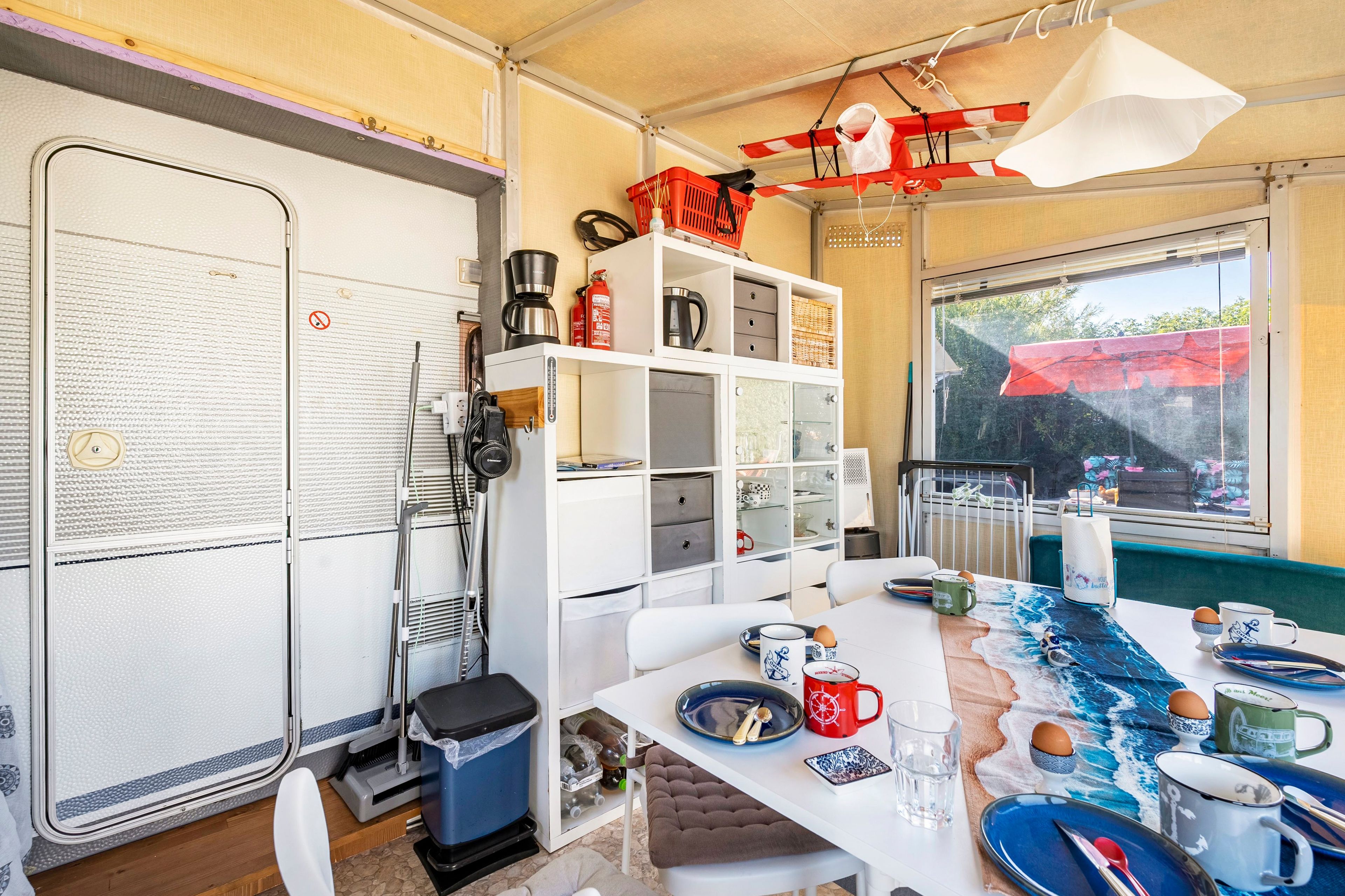 A compact kitchen with a dining area, equipped with a coffee maker, a kettle, and a trash bin.