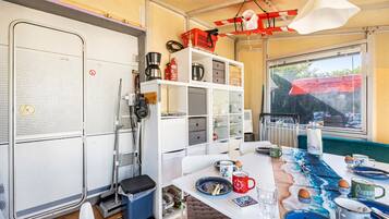 A compact kitchen with a dining area, equipped with a coffee maker, a kettle, and a trash bin.