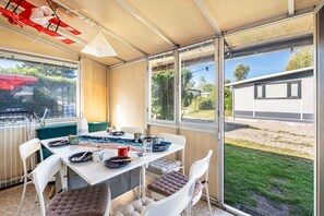 Uma área de refeições coberta ao ar livre, com uma mesa posta para dois, cadeiras e vista para o jardim.