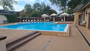 Une piscine rectangulaire bordée de briques, entourée d’une terrasse également en briques. On y trouve des chaises longues et des parasols, et une clôture en bois en arrière-plan.