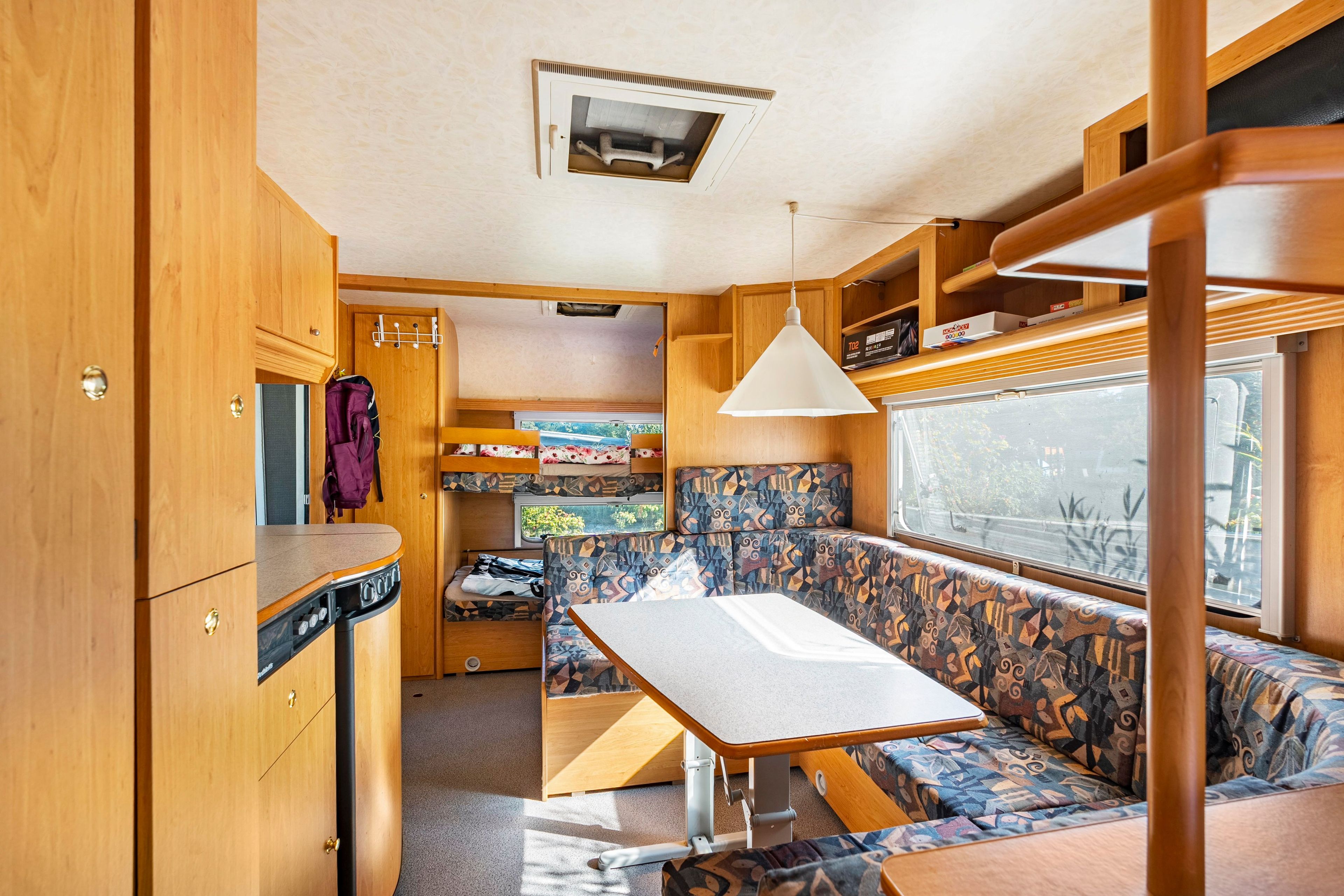 A compact RV interior with a kitchenette, a dining area, and a seating space with a view.