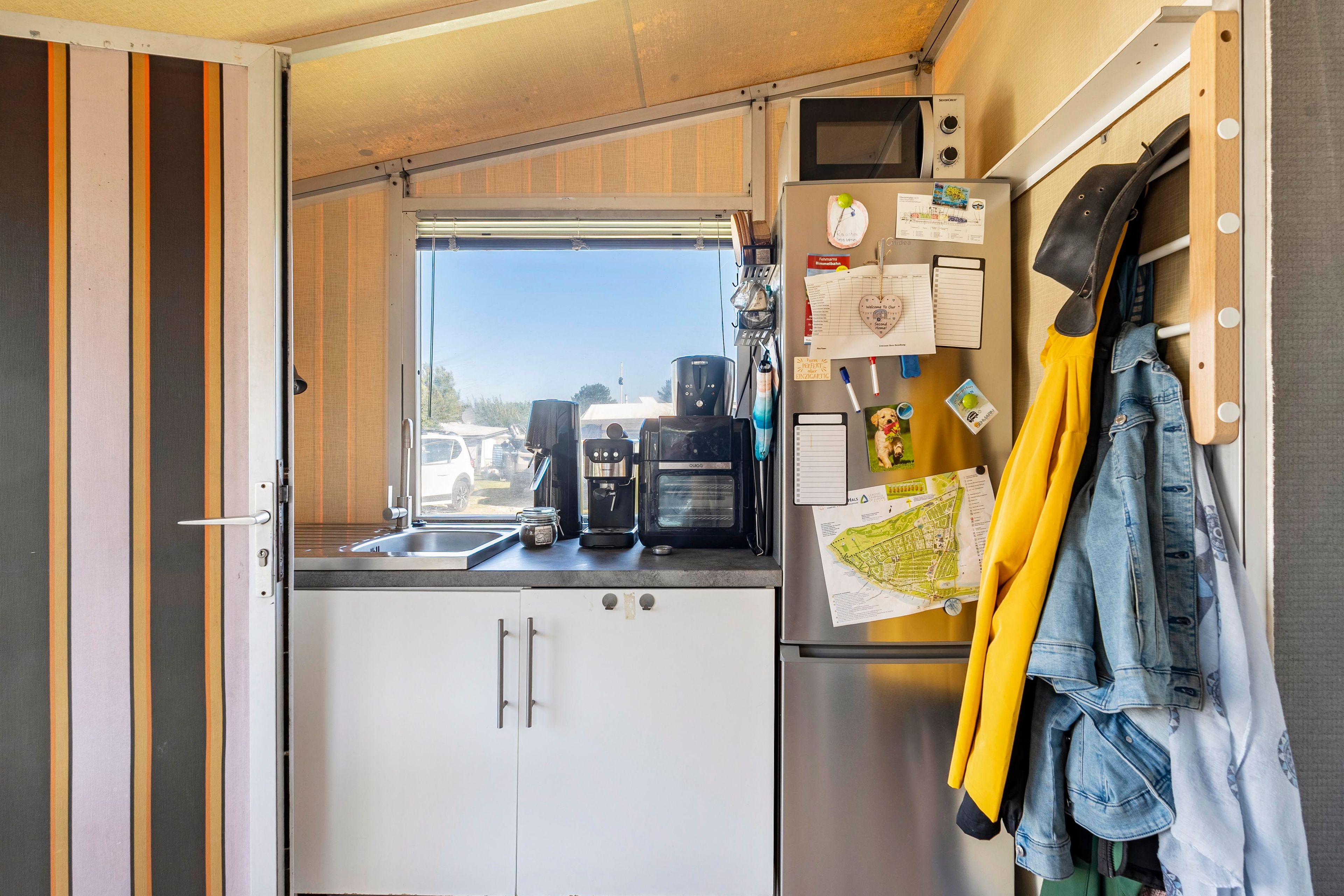 A compact kitchen with a refrigerator, coffee maker, and a window with a view of the outside.
