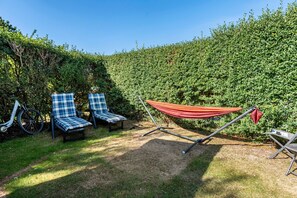 A garden area with two blue and white checkered lounge chairs, a red hammock, and a bicycle.