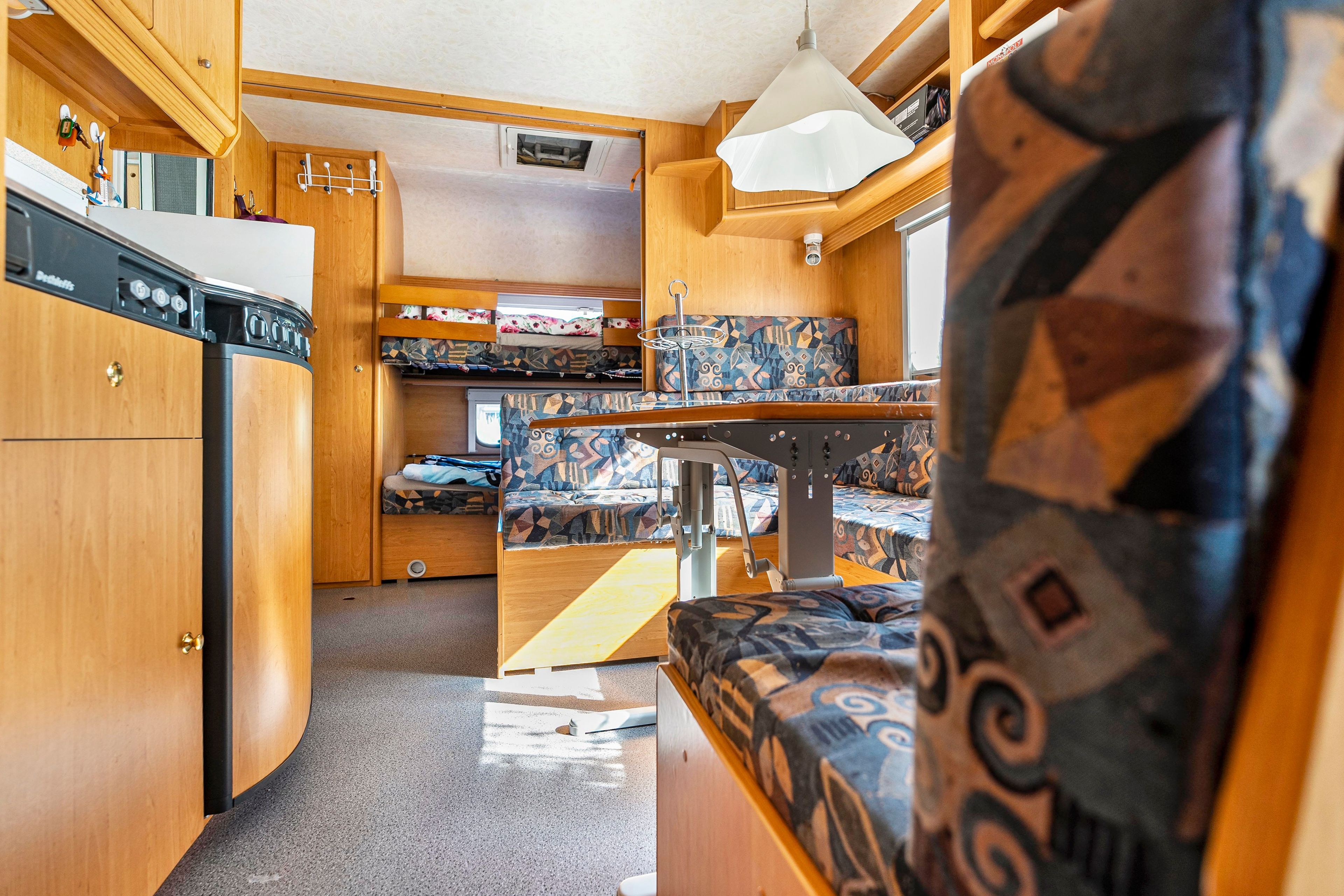 Interior compacto de una autocaravana, con kitchenette, zona de comedor y litera.