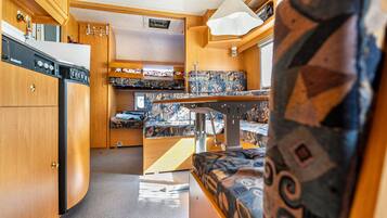 Interior compacto de una autocaravana, con kitchenette, zona de comedor y litera.
