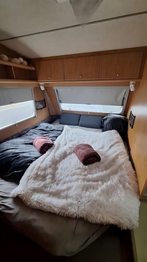Ein gemütliches Wohnmobil-Interieur mit Bett, Staufächern und einem Fenster.