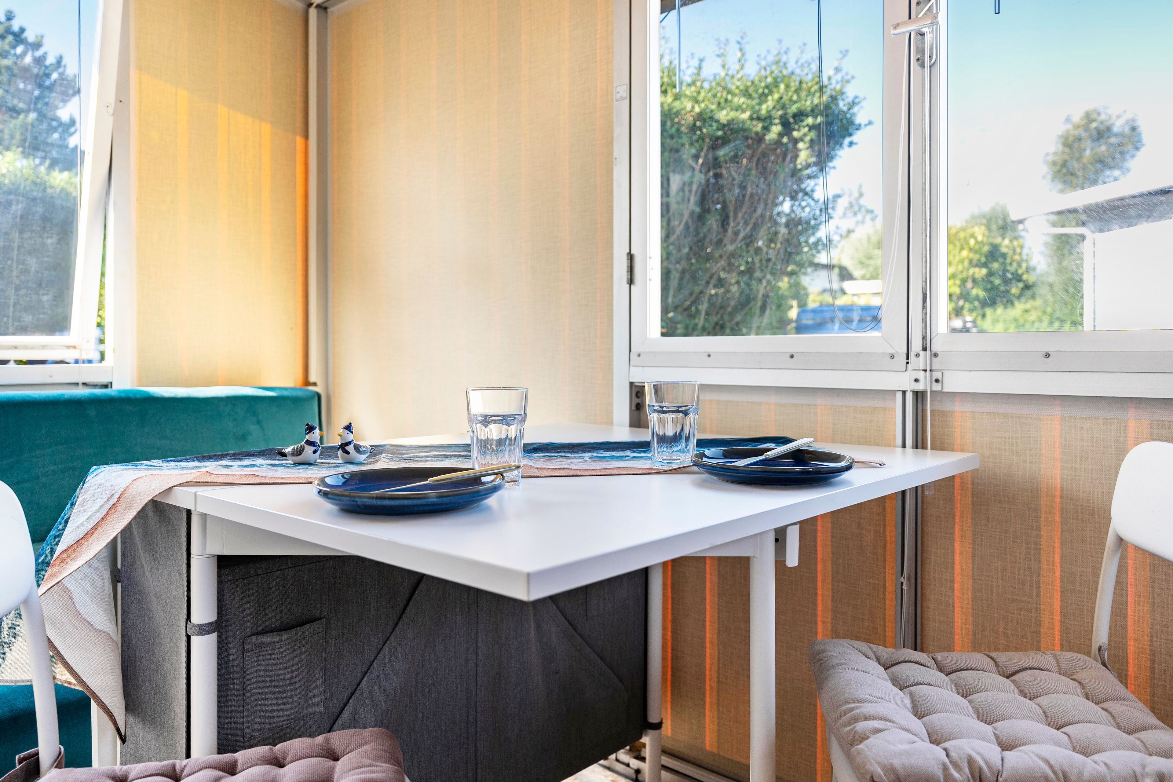 A compact room with a small table set for two, a window with a view of trees, and a bench.