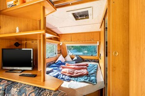 Un intérieur de camping-car compact comprenant un lit, un téléviseur et une petite table.