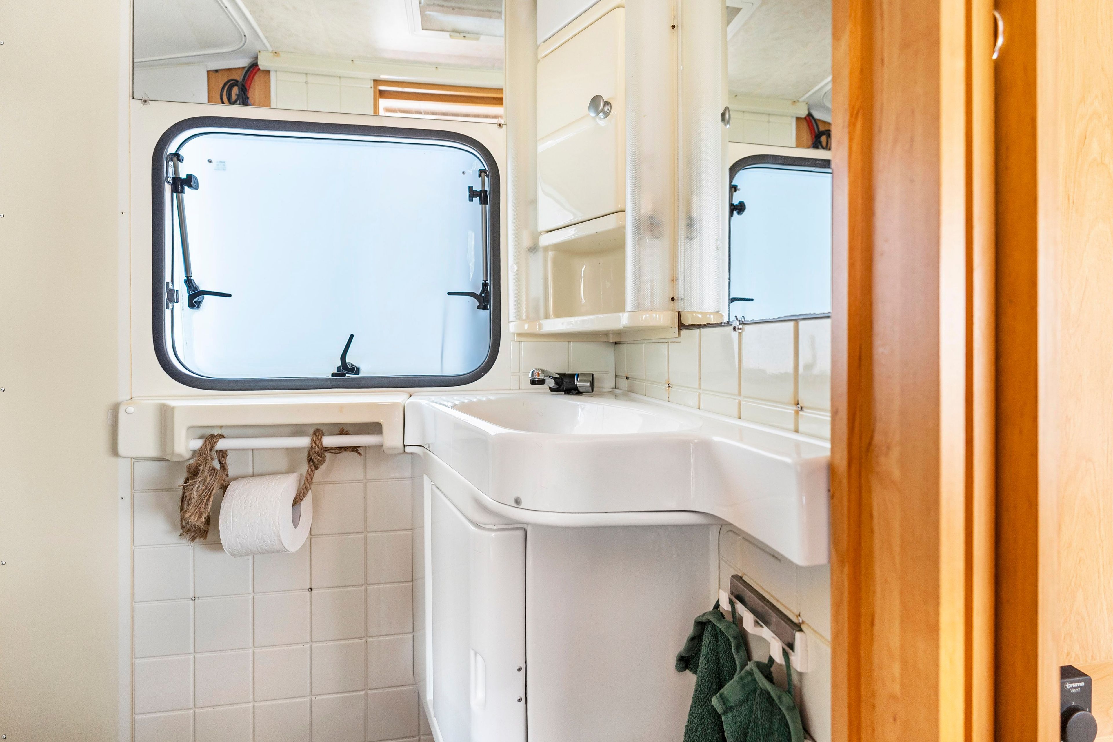 Ein kleines Badezimmer mit Fenster, Waschbecken und Spiegel.