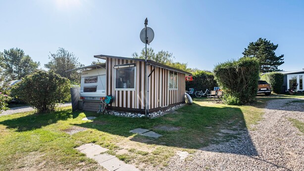 Una casa móvil con antena parabólica, una estructura pequeña adosada y un camino de grava que la conduce.