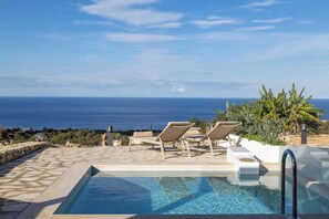 Piscina con sillones de descanso y vista al mar.
