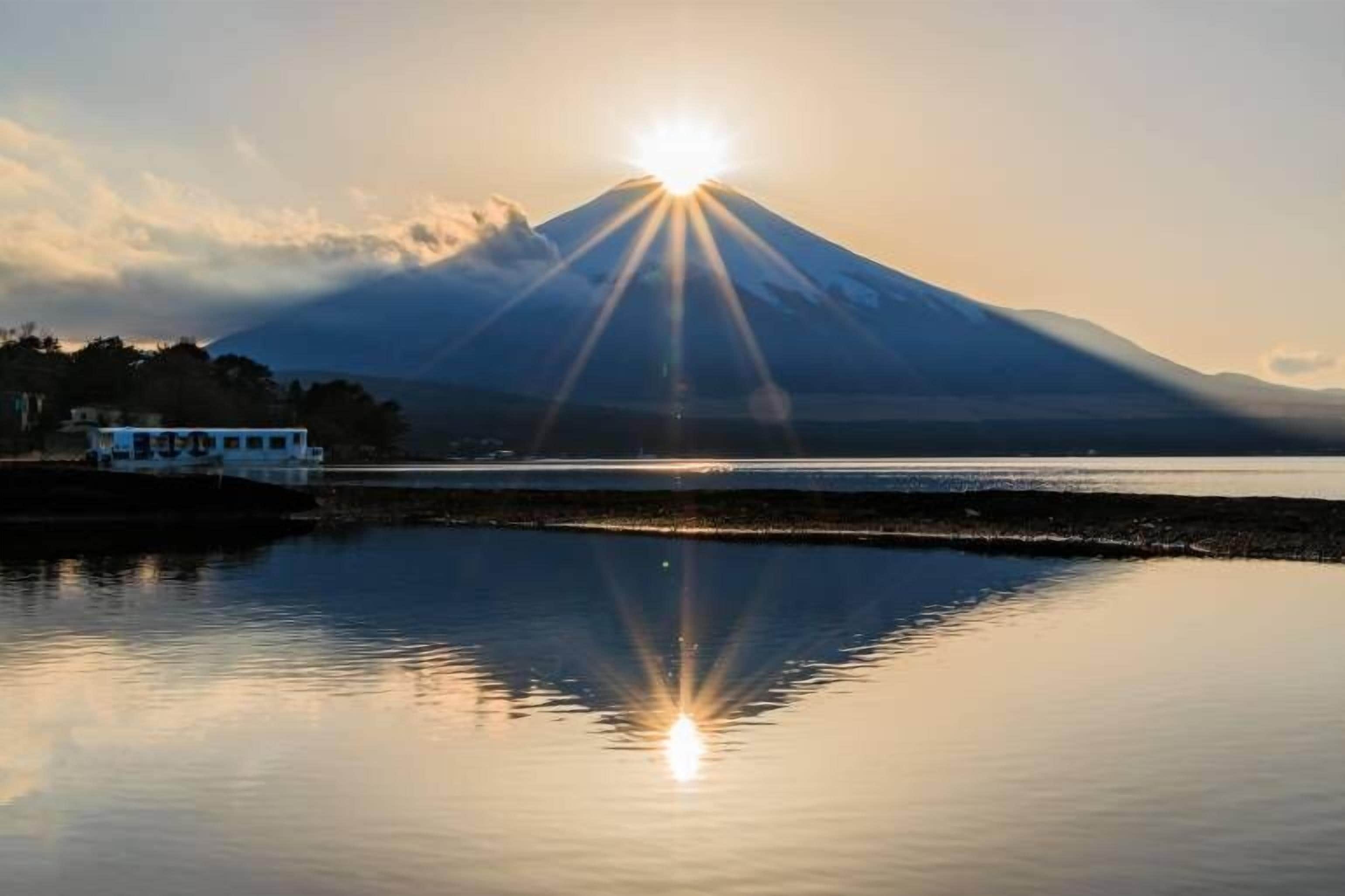 A calm lake with a mountain in the background and a building on the left.