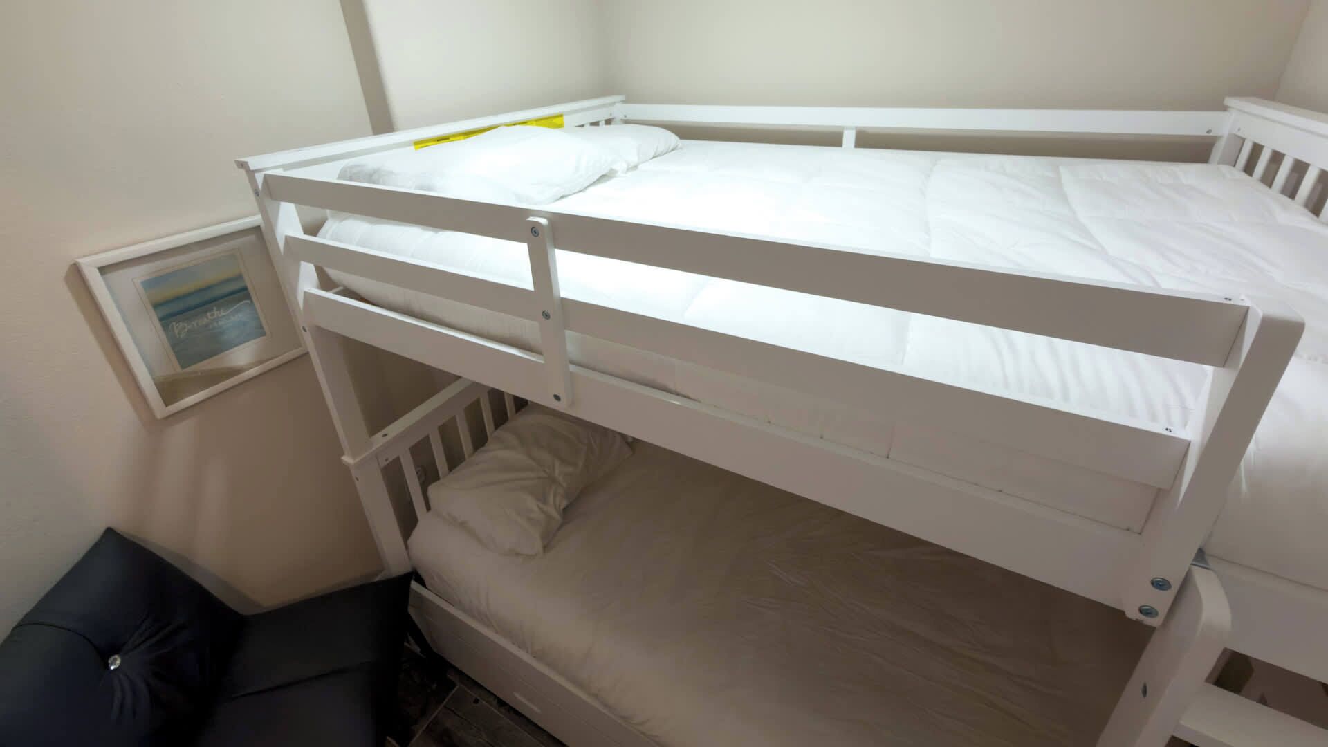Ein Stockbett mit weißer Bettwäsche in einem Zimmer mit kleinem Fenster und einem gerahmten Bild an der Wand.
