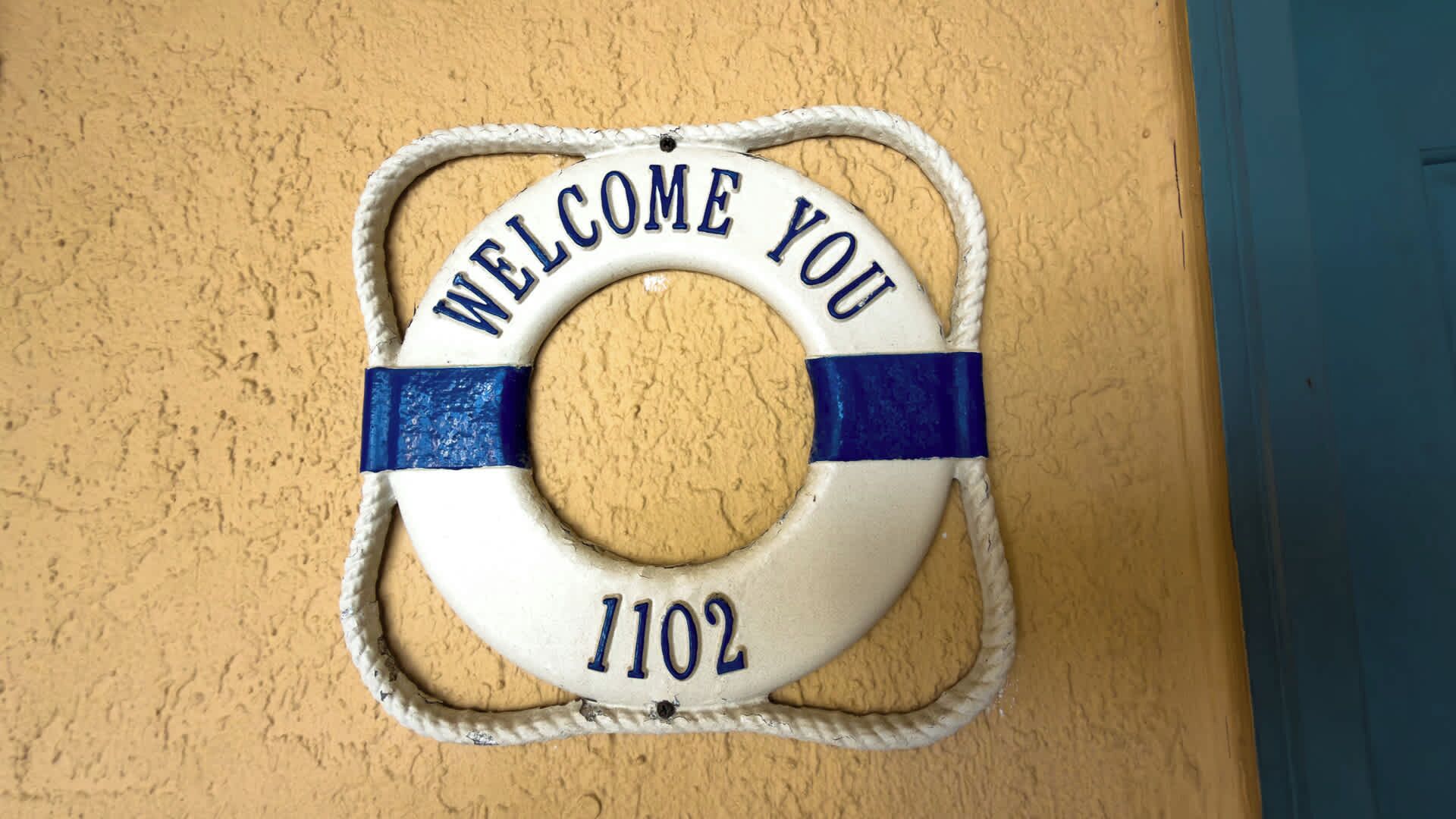 Une bouée de sauvetage sur laquelle on peut lire « BIENVENUE » et le numéro « 1102 », le tout placé sur un mur texturé.