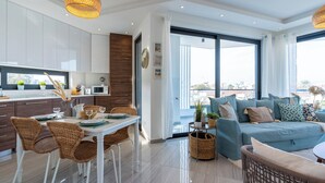 Ein modernes Wohnzimmer mit einem blauen Sofa, Korbstühlen und einem Essbereich mit einem weißen Tisch.