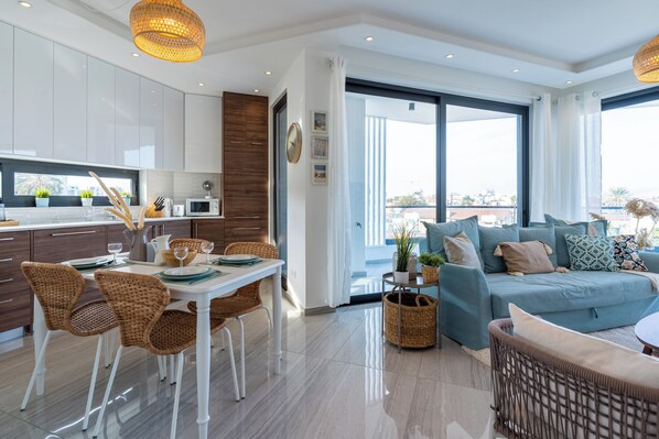 A modern living room with a blue sofa, wicker chairs, and a dining area with a white table. - Thálassa 2-BR Apt. & Balcony in Larnaca (Larnaca)