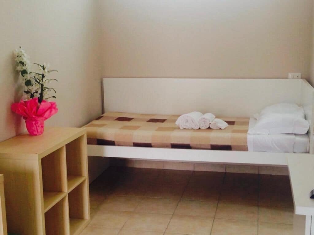 A single bed with a checkered bedspread, a bedside table, and a small shelf unit.
