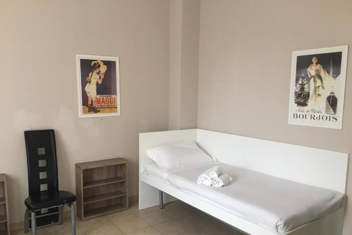 A small, clean room with a single bed, a chair, and two posters on the wall.