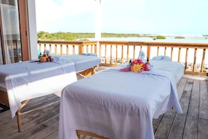 Deux tables de massage sur une terrasse en bois, avec vue sur une plage et l’océan.