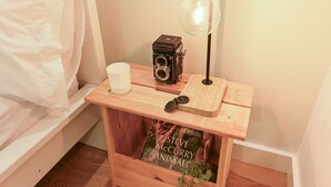 A wooden bedside table with a vintage camera, a pair of sunglasses, a white cup, and a book titled 'Steve McCurry: Animals'. - ON Apartments - MA62 (Porto)