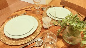 A wooden dining table with a woven placemat, a glass vase with green foliage, and a candle holder. - ON Apartments - MA62 (Porto)