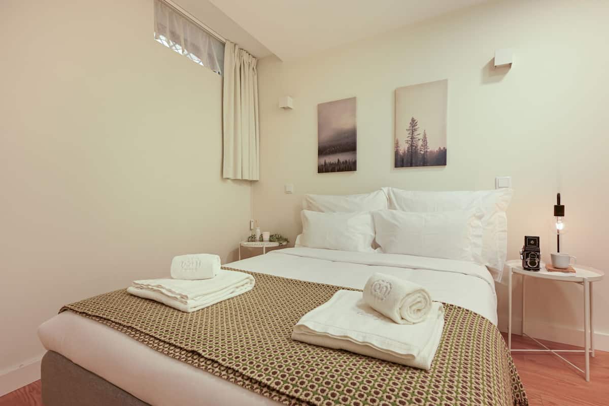A hotel room with a bed, a bedside table with a lamp, and two wall-mounted paintings.