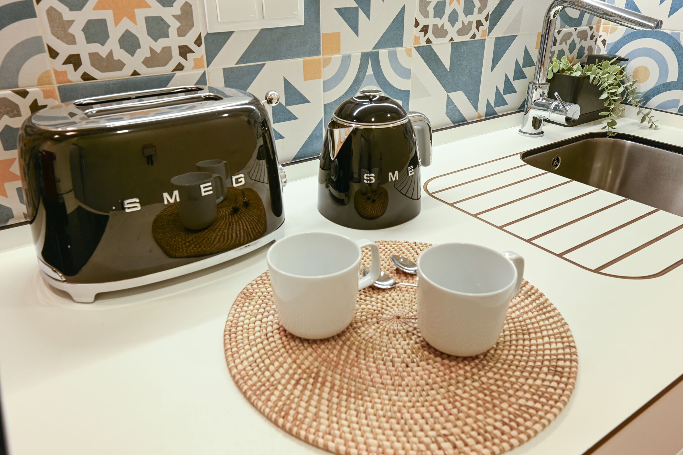 Eine Küche mit einem Toaster, einer Kaffeemaschine und zwei Tassen auf einer gewebten Unterlage.