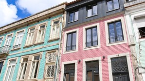 A row of colorful buildings with distinct architectural styles, including a pink brick building with a black door and a teal building with a decorative window grille. - ON Apartments - MA62 (Porto)
