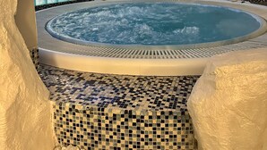 Una vasca idromassaggio con pavimento e pareti in mosaico, circondata da pareti bianche strutturate e una finestra con vetro azzurro.
