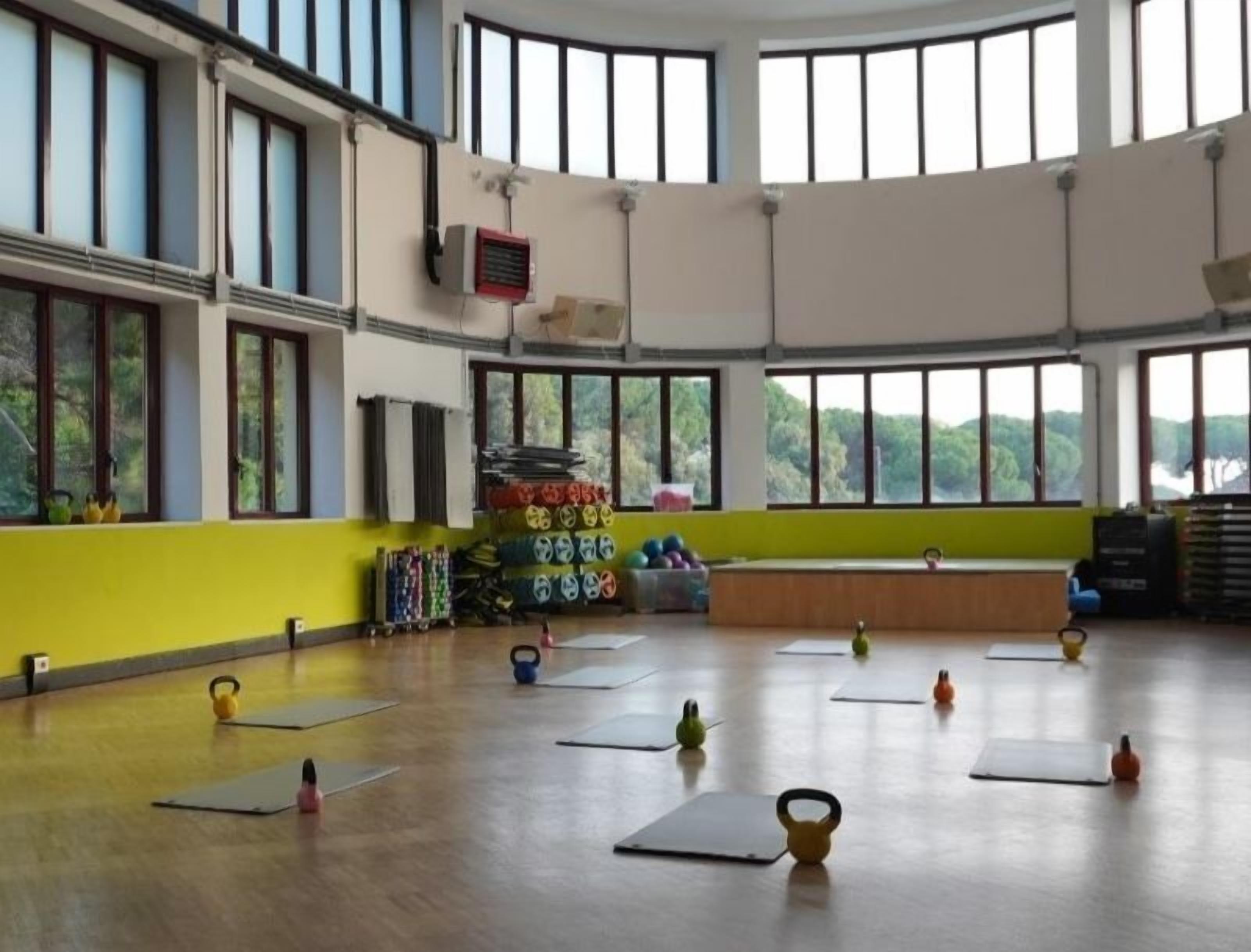 A spacious indoor gym with large windows, yoga mats, and kettlebells arranged on the floor.