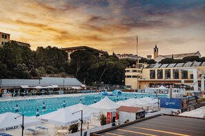 A swimming pool area with lounge chairs and umbrellas, surrounded by buildings and trees. - Arena Albaro House (Genoa)