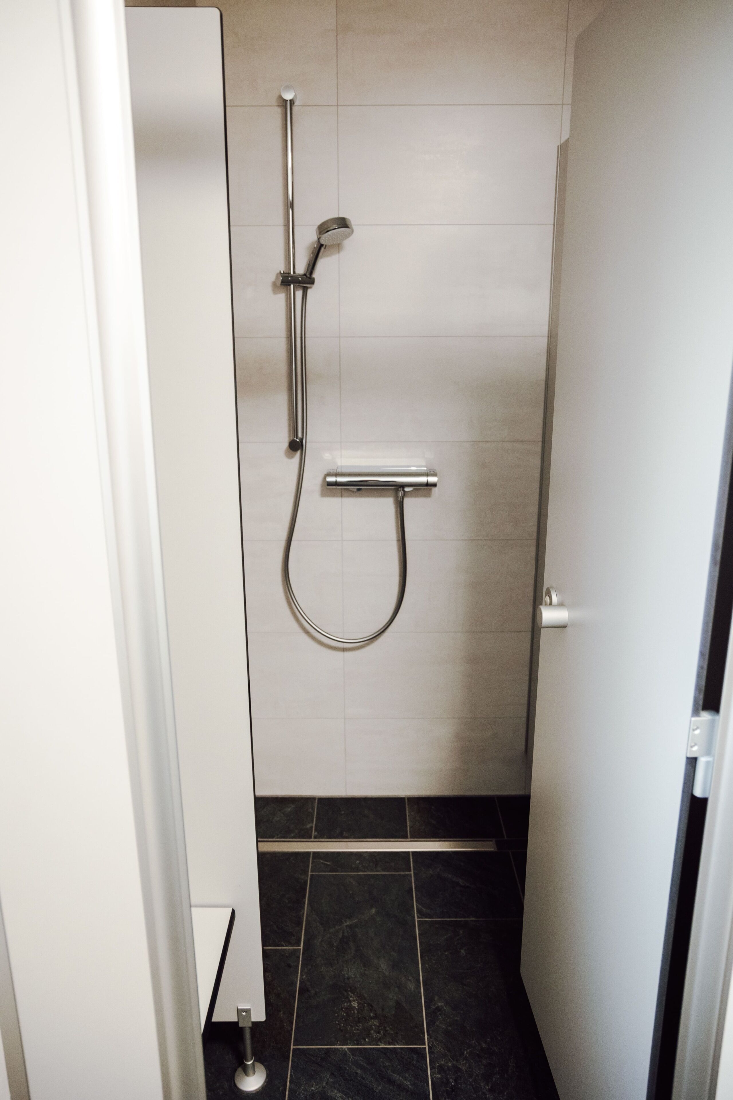 A small, modern bathroom with a shower, tiled walls, and a dark floor.