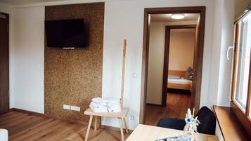 Een hotelkamer met een houten vloer, een televisie bevestigd aan een kurkwand, een klein houten tafeltje met handdoeken, en een bed met een houten hoofdeinde.