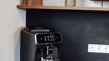 A coffee machine on a black countertop with a wooden shelf above it.