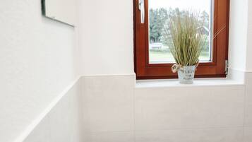 A bathroom with a white sink, a window with a wooden frame, and a potted plant on the windowsill.
