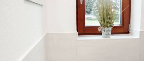 A bathroom with a white sink, a window with a wooden frame, and a potted plant on the windowsill.