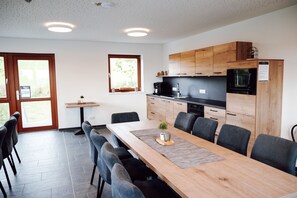 Une cuisine moderne avec des meubles en bois, un micro-ondes noir et un coin repas comprenant une longue table et des chaises.