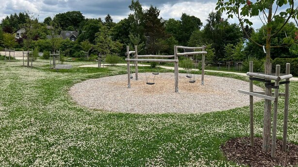 A playground with swings and a circular seating area surrounded by a gravel path. - Das Fränkische Reichenbach (Reichenbach)