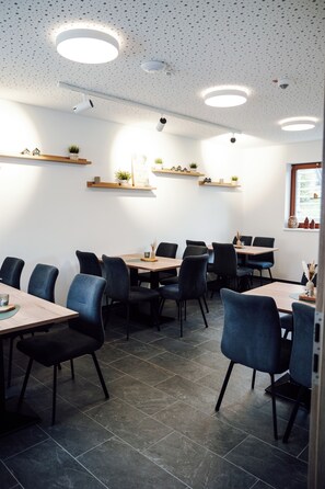 A modern dining area with round tables and chairs, ceiling lights, and wall-mounted shelves with plants. - Das Fränkische Reichenbach (Reichenbach)